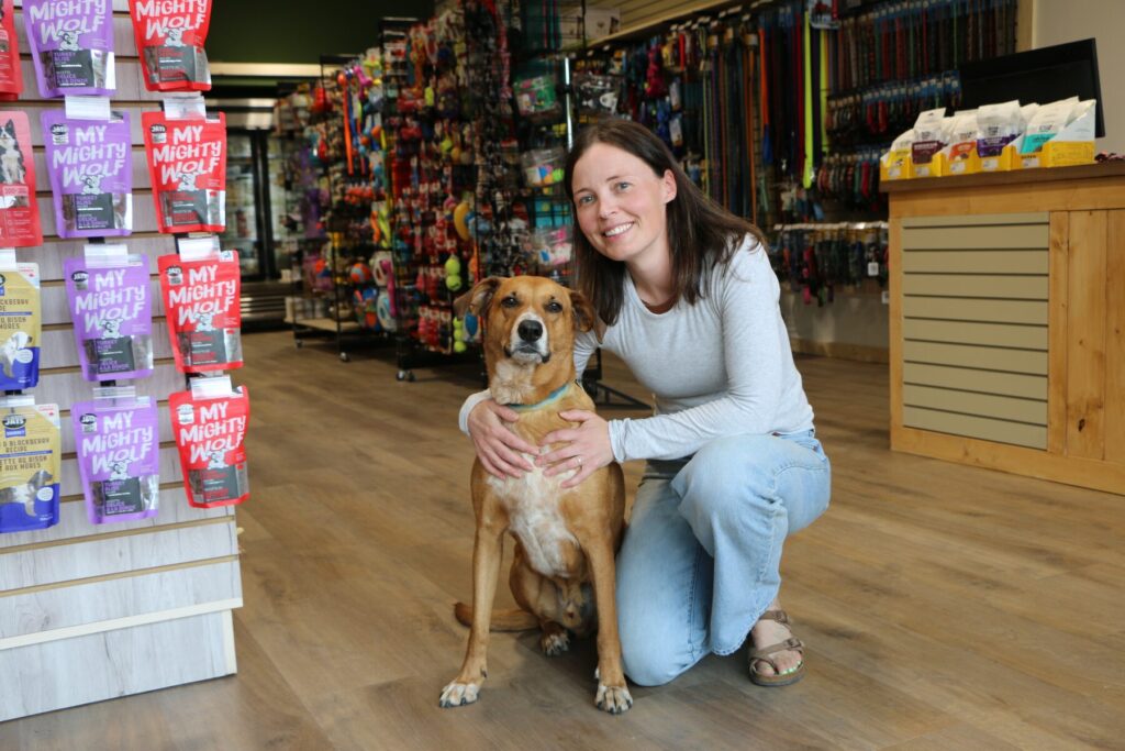 Paw Shop team member kneeling beside a friendly dog inside the new Cranbrook store